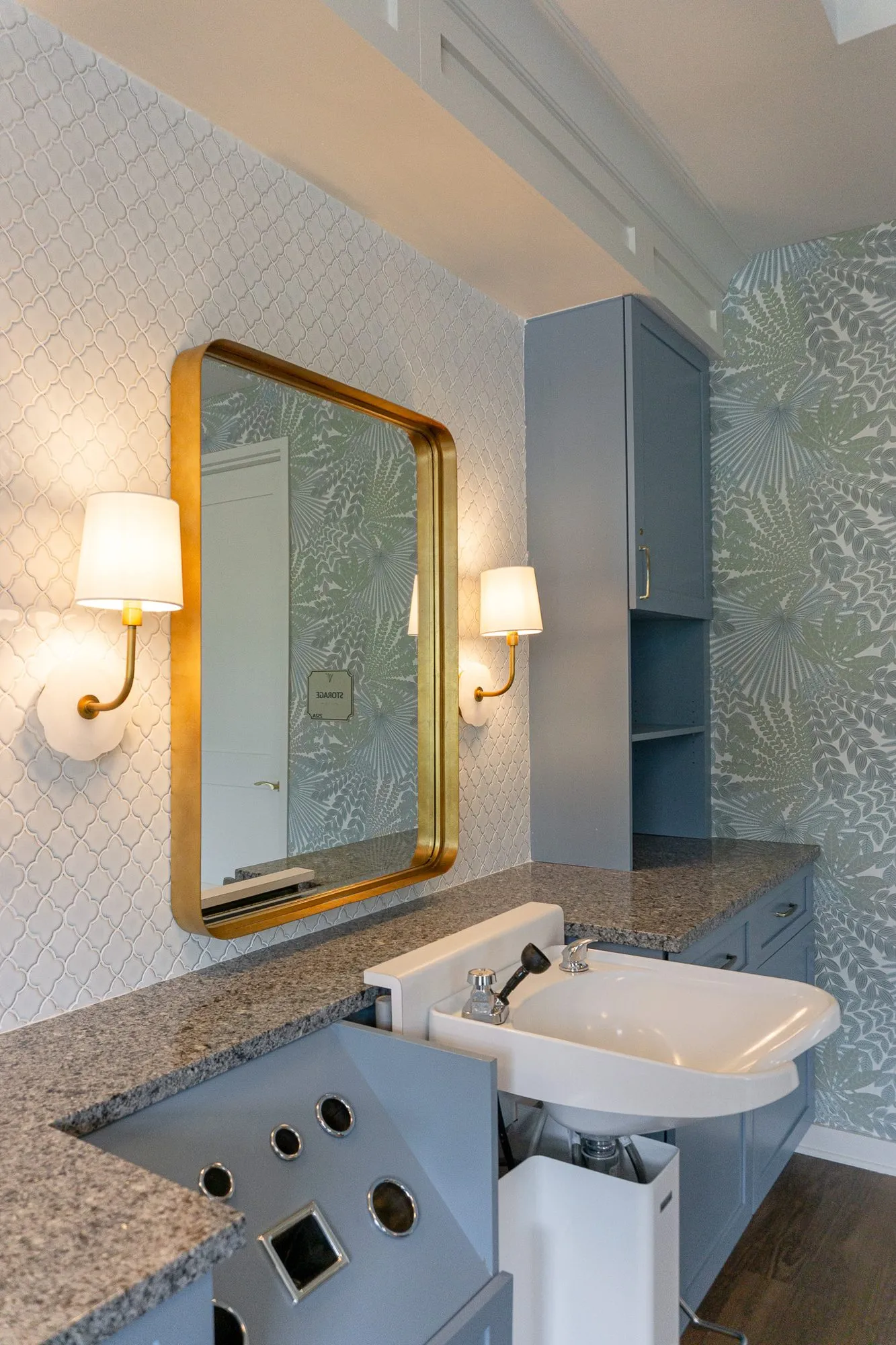 Senior living salon shampoo bowl and granite counter below a brass-framed mirror on white arabesque tile