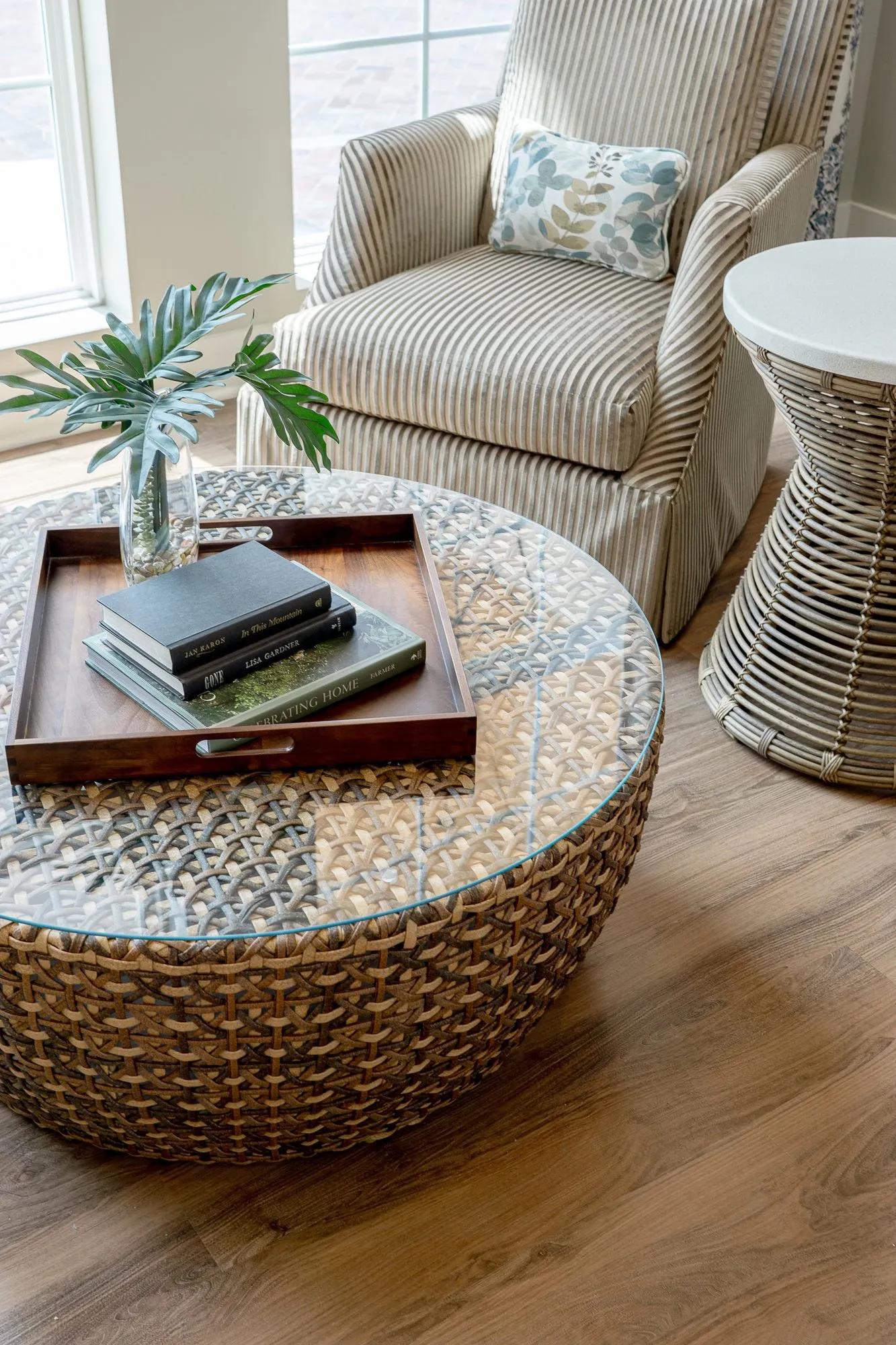 Senior living sitting room with a sunlit striped armchair and leaf print pillow beside a rattan table, a woven drum table
