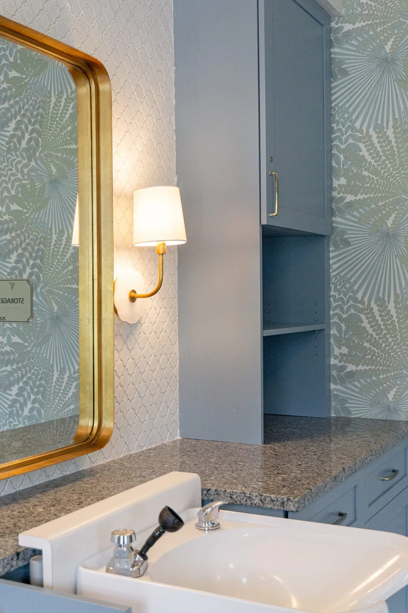 Senior living salon shampoo bowl below a brass mirror and sconce, palm frond wallpaper beyond