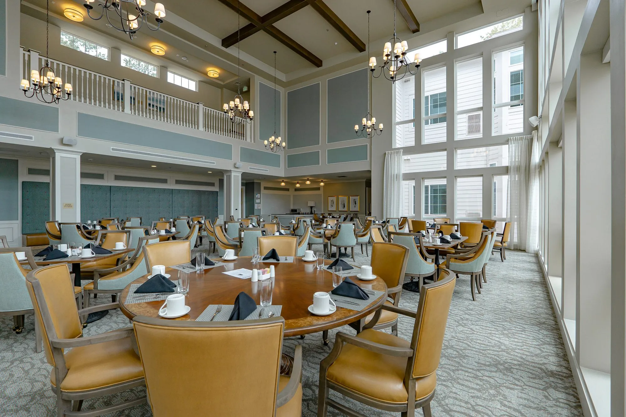 Senior living dining room with a round table for eight and camel leather chairs along the window wall