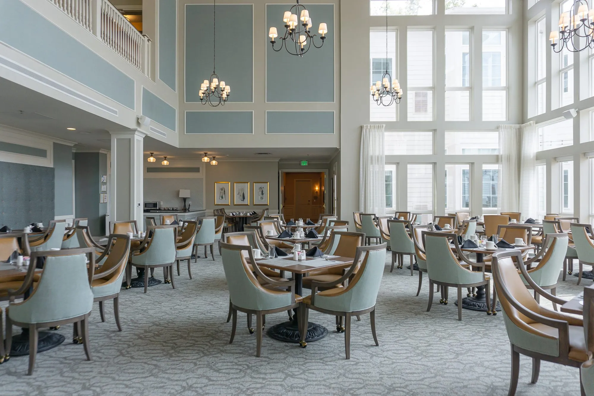 Senior living dining room centred on the far wall's wood door and framed prints, candle chandeliers and the balcony above