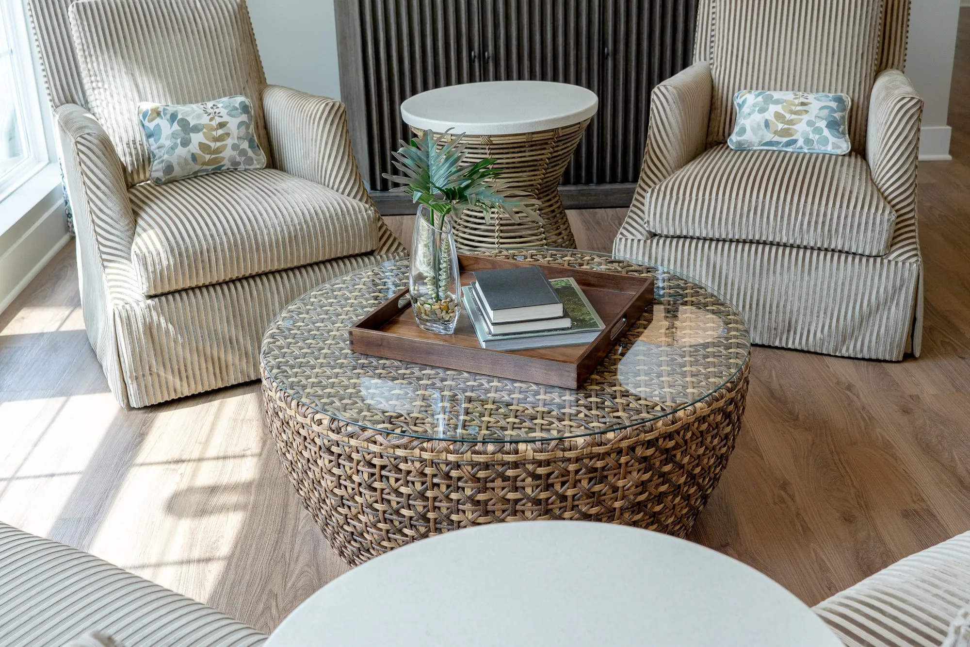 Senior living sitting room with a glass-topped woven coffee table and books between two striped skirted armchairs