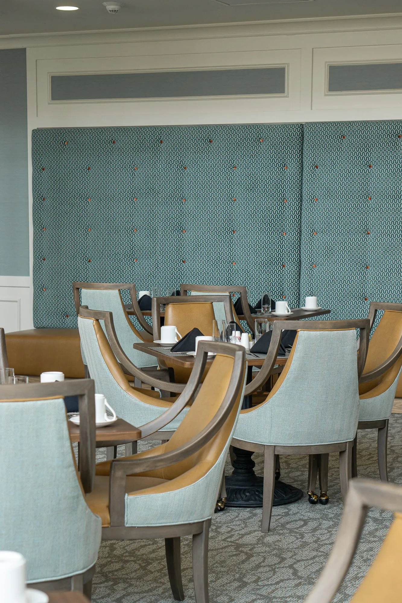 Senior living dining room with sage and camel chairs before a quilted sage upholstered wall