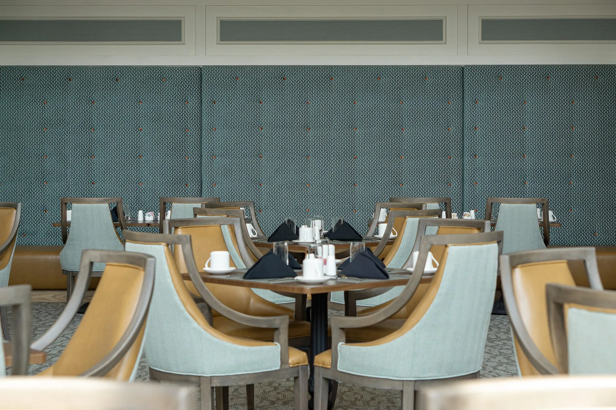 Senior living dining room with a table set for four before a tall quilted sage wall, sage and camel chairs around it