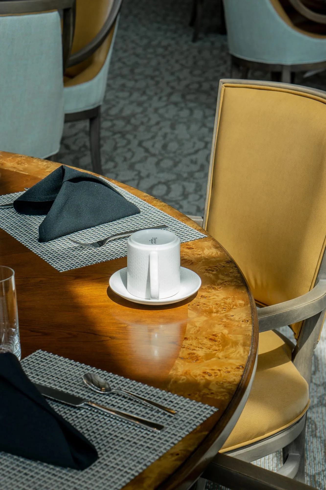 Senior living interior detail: set burl wood table with black napkins and a white cup, a camel chair alongside