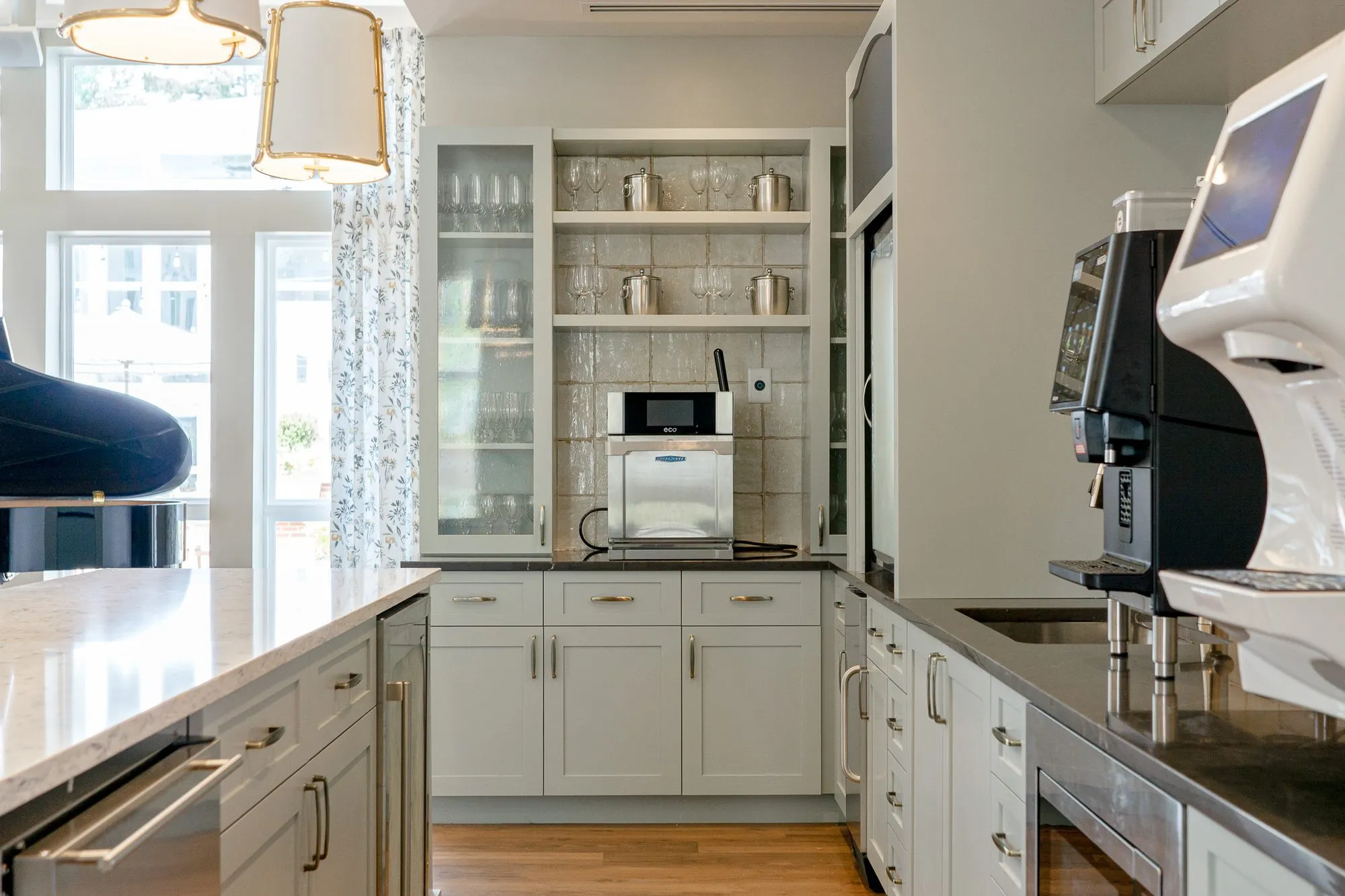 Senior living kitchen with white shaker cabinets, glass-front uppers holding glassware and a coffee machine on the counter