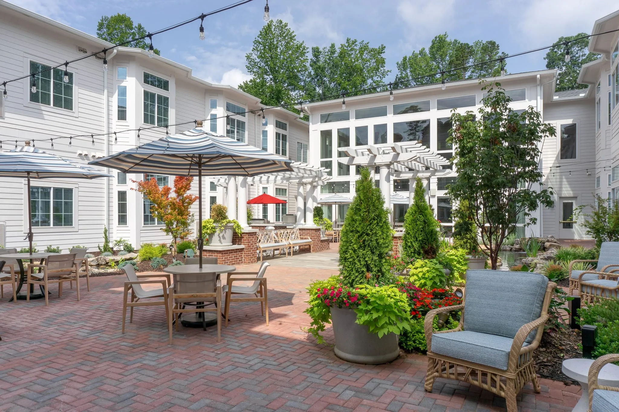 Senior living central courtyard with white pergolas and string lights over brick paving, planters and patio seating