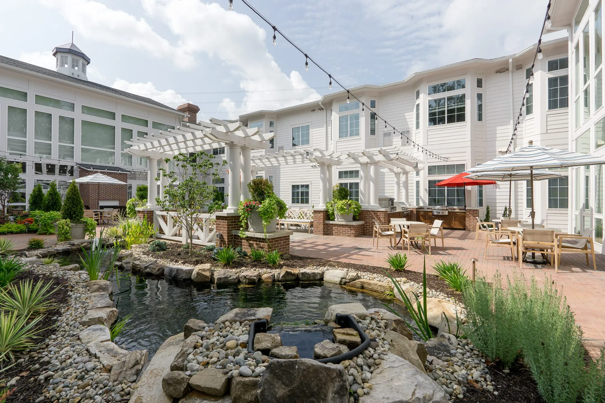 Senior living courtyard water feature, a stone-edged pond and grasses in front of the pergola