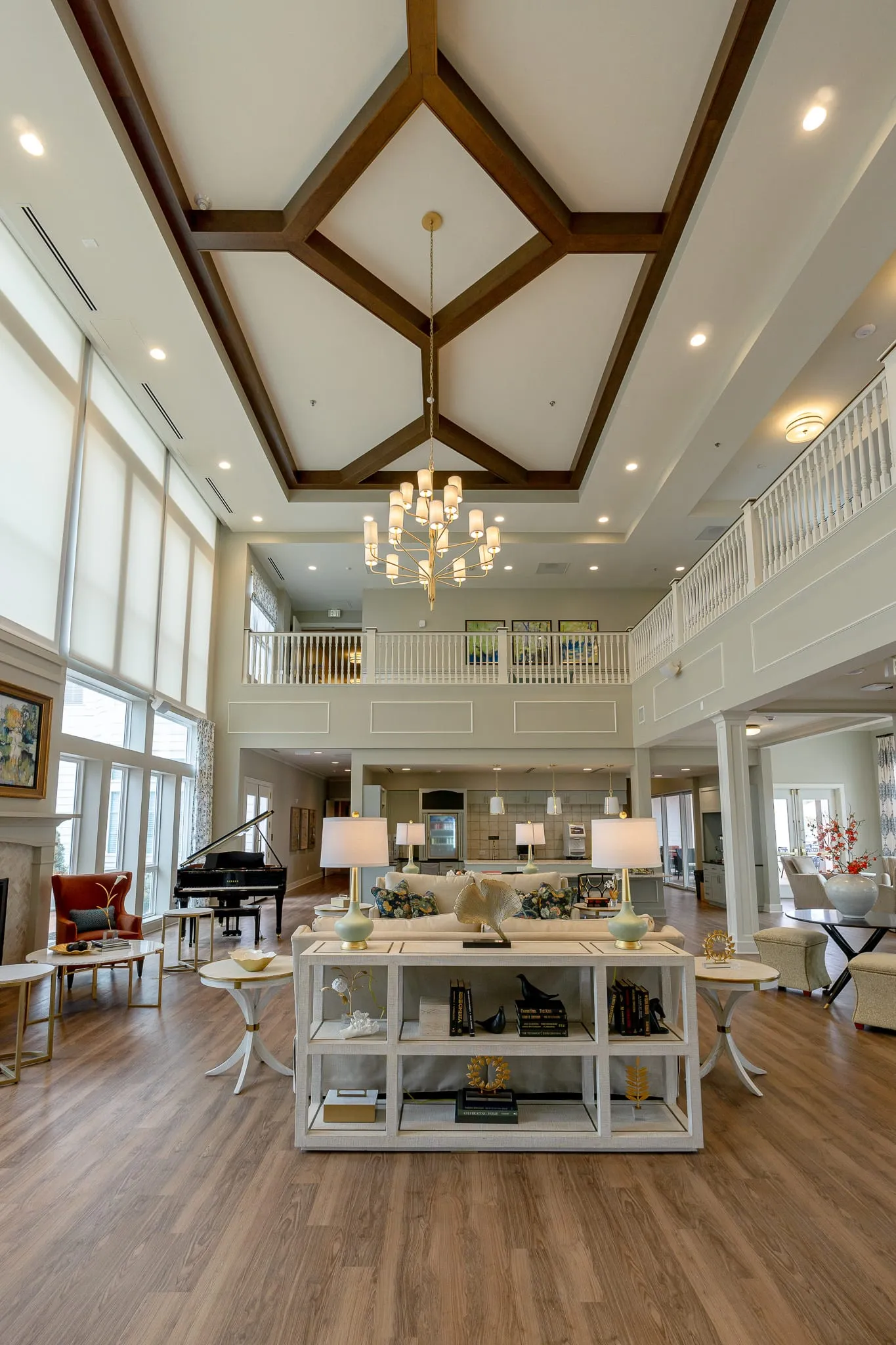 Senior living great room seen from the second-floor terrace, a wood-beamed ceiling and chandelier above the grand piano