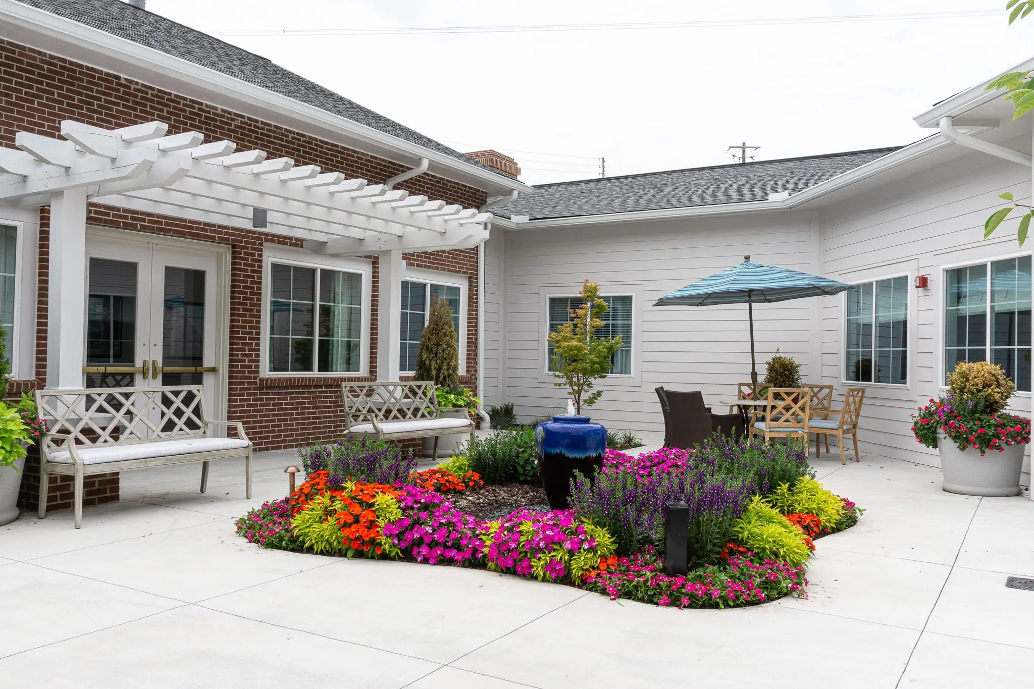 Senior living memory care courtyard with a white pergola over the patio beside a bed of flowering annuals