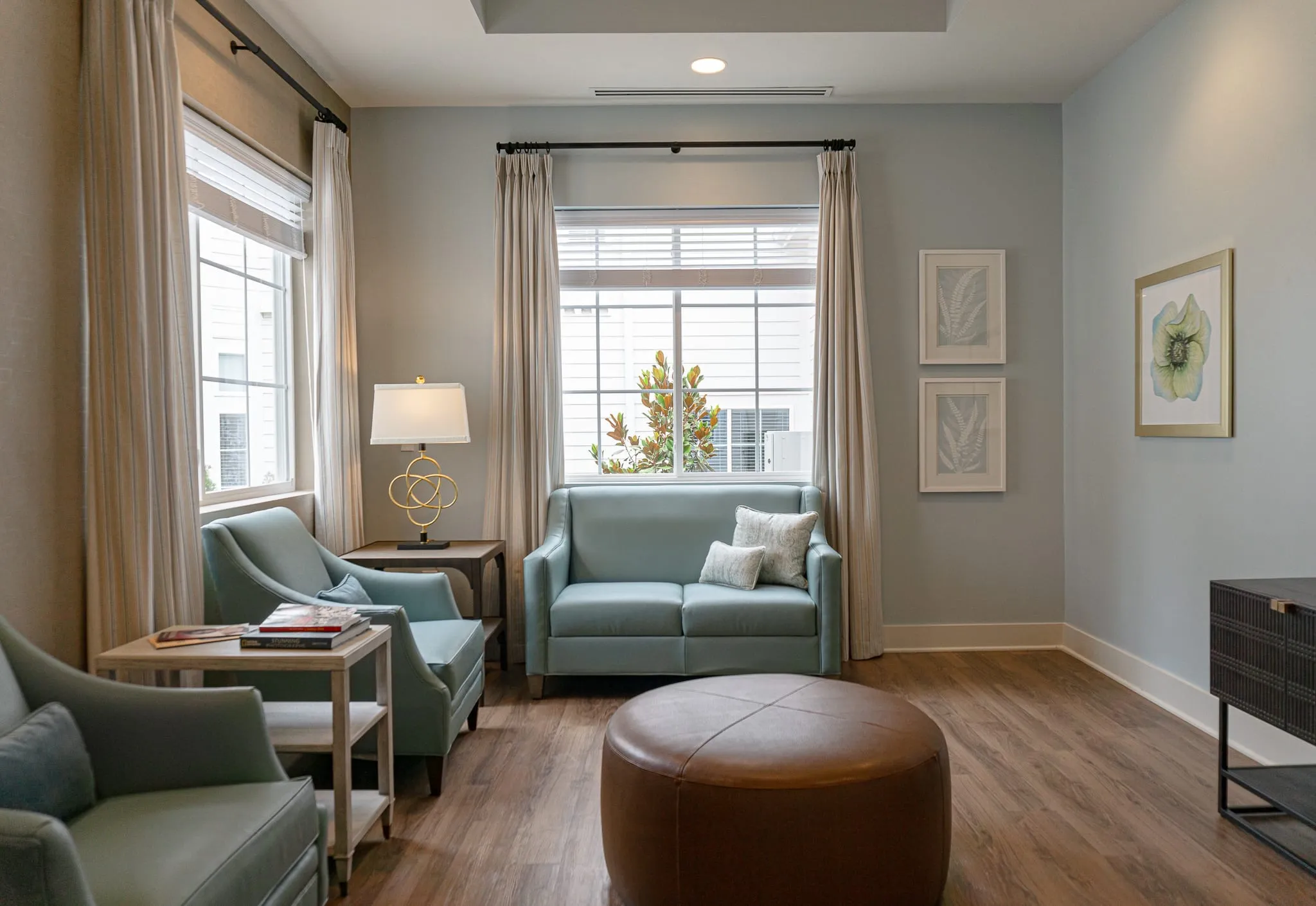 Senior living residence sitting room with sage upholstered chairs and loveseat around a leather ottoman