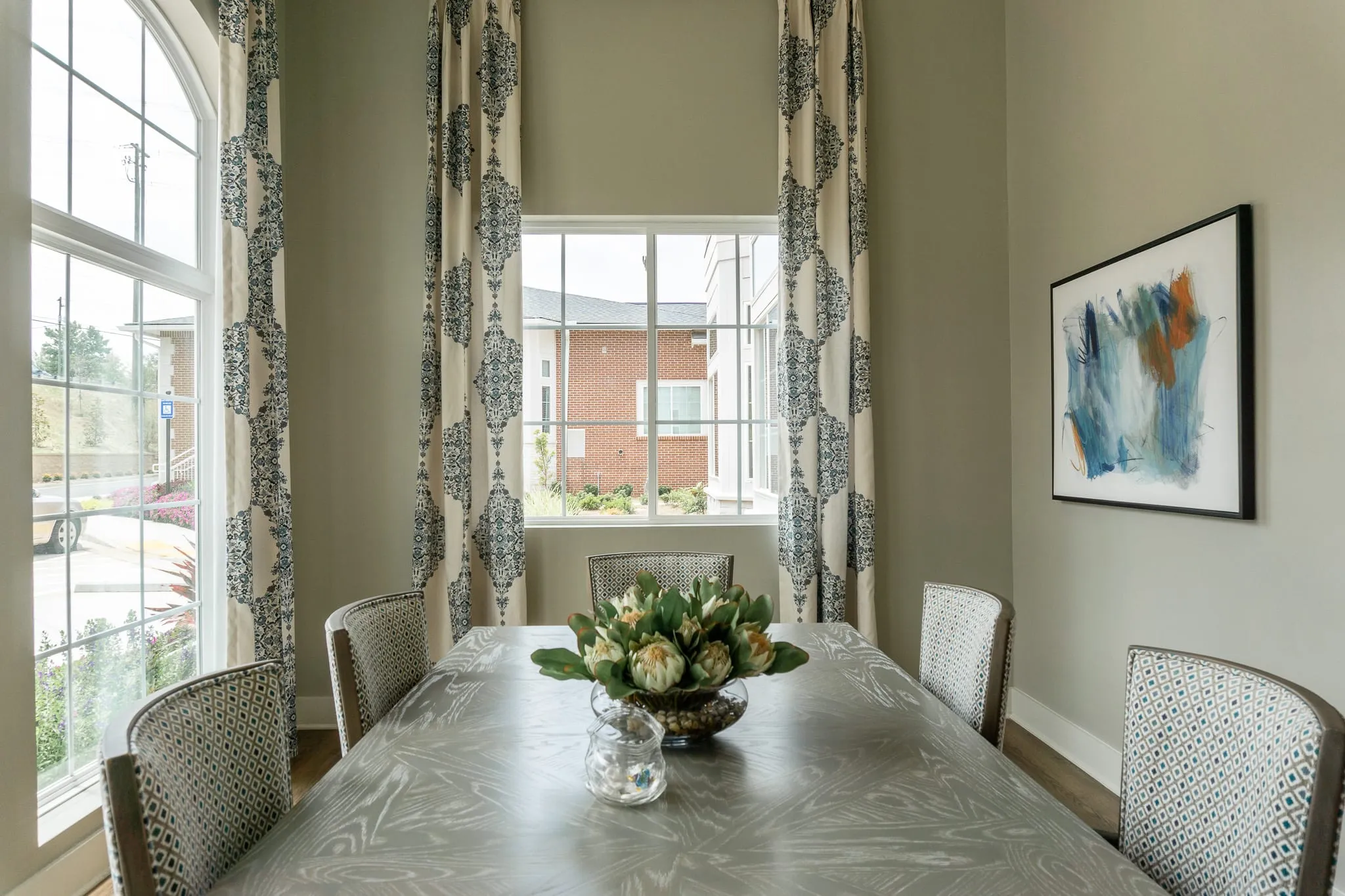 Senior living private dining room with patterned chairs at a long table beside tall windows framed in patterned drapery