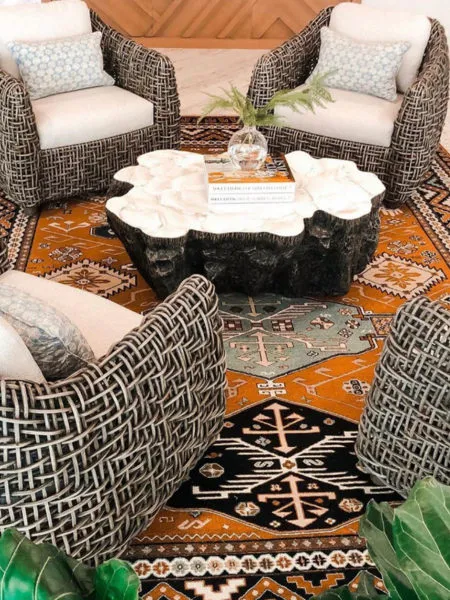 Four black and white woven barrel chairs drawn around an organic stone coffee table on layered orange and navy patterned rugs